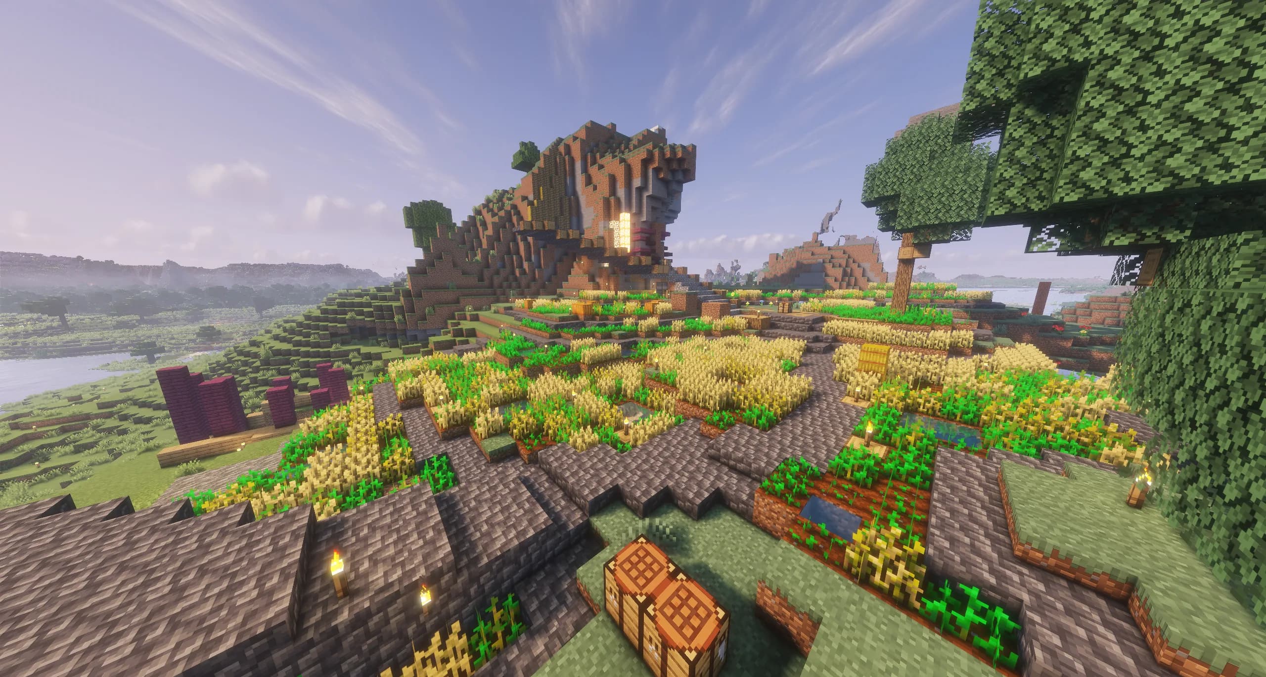 A member's hillside farm: terraced wheat fields and stone paths climbing to a house built into a rocky outcrop, with lakes and hills beyond.
