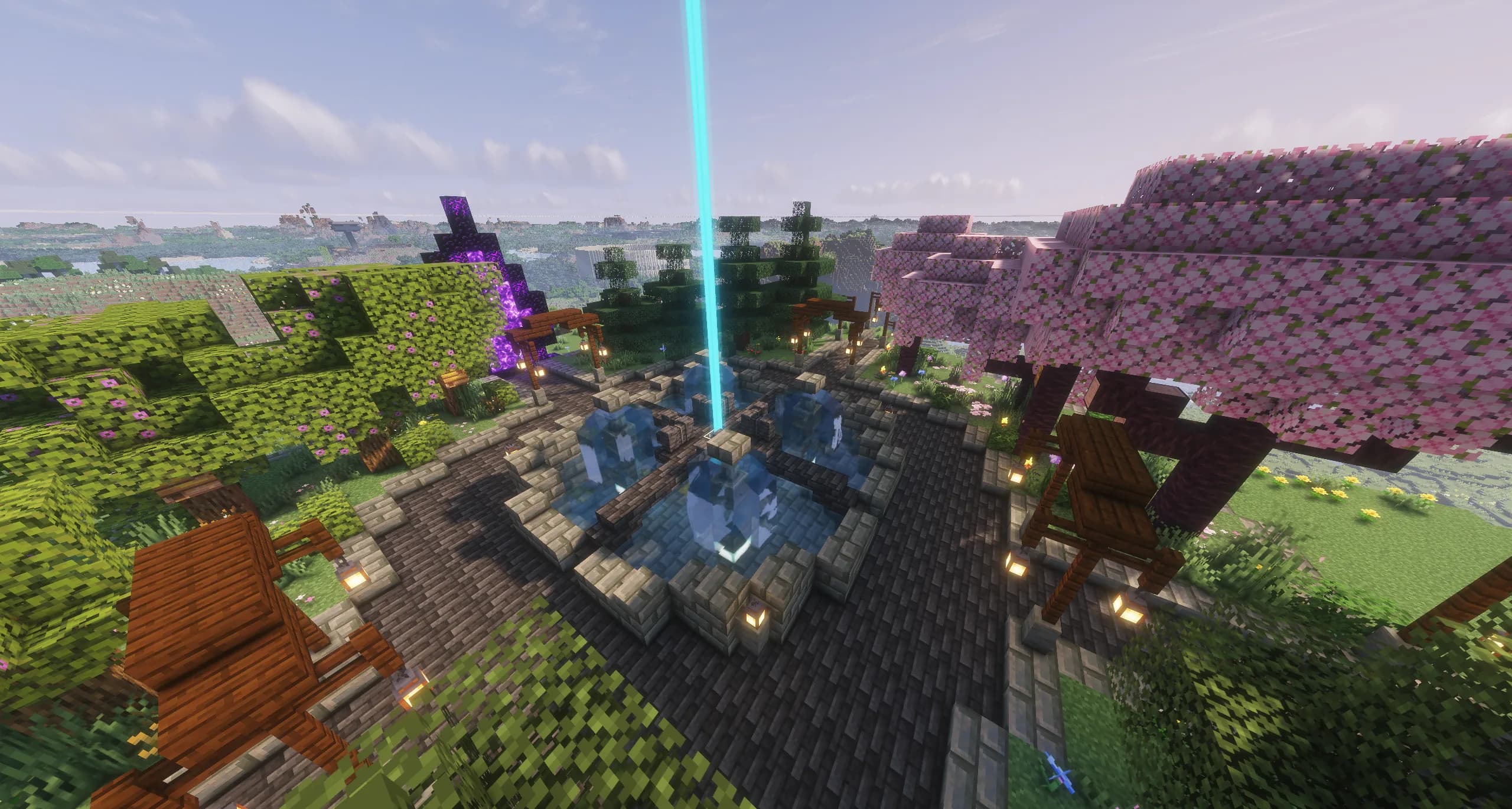 Spawn's stone plaza from above: a fountain with a beacon rising from it, lantern-lit paths, cherry and azalea trees, a Nether portal, and the world stretching to the horizon.