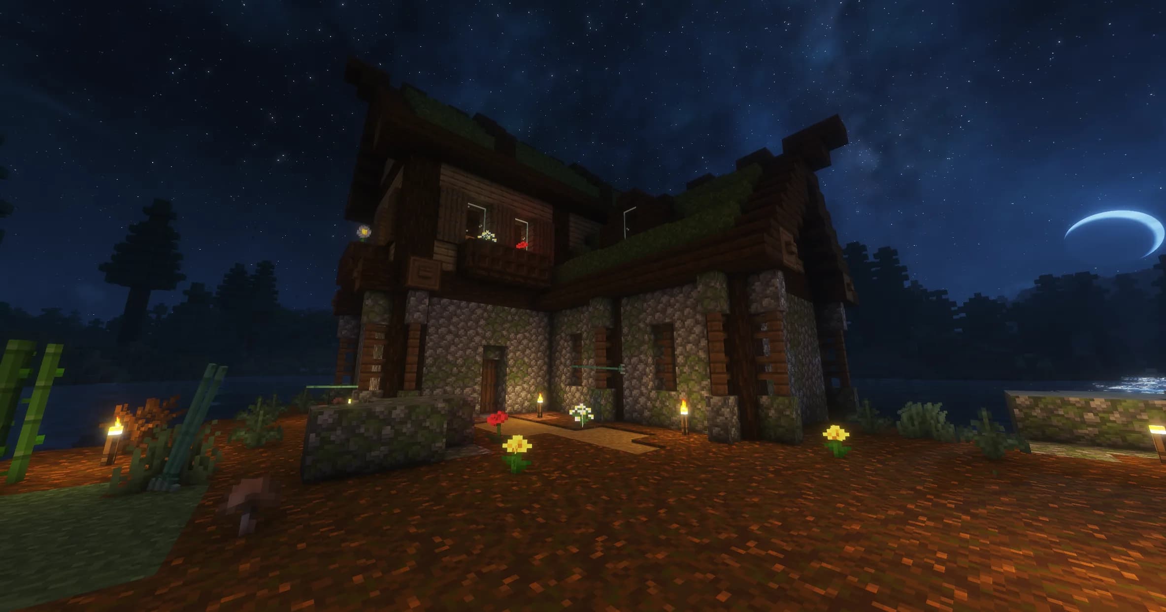 A two-storey house of mossy stone and dark timber at night, with a turf roof, flowers along the path and torches by the door.