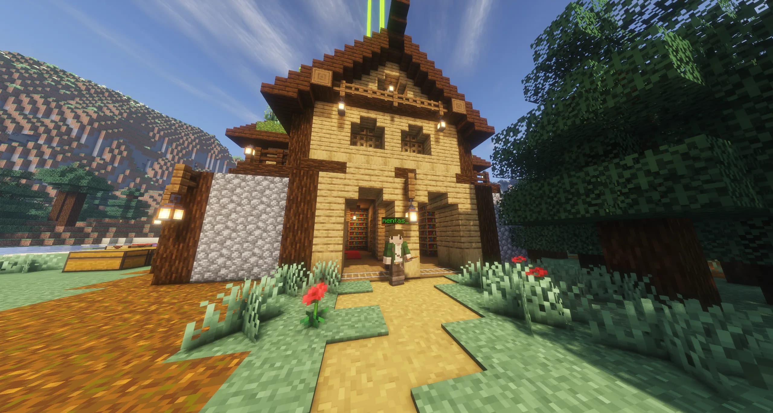 A tall timber library with bookshelves inside and lanterns by the door, with its builder standing in the doorway under a blue sky.